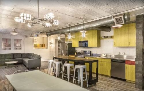 Modern kitchen and living area with industrial decor, featuring yellow cabinets, stainless steel appliances, and a cozy sofa.