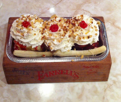 A banana split with three scoops of ice cream, topped with whipped cream, nuts, and cherries, served in a wooden dish.