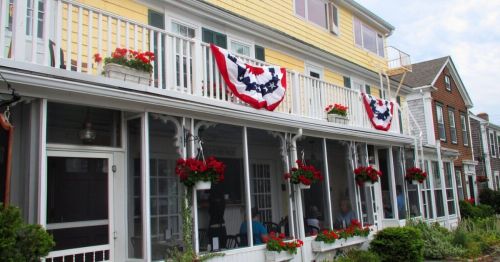 A charming house with a yellow exterior, decorated with red flowers and patriotic bunting on the porch.