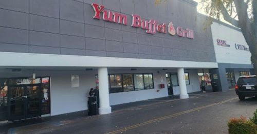 Exterior of Yum Buffet Grill restaurant, featuring a large sign and windows, with a parking lot in front.