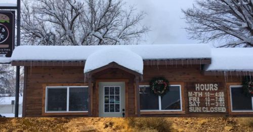 A cozy wooden café covered in snow, with icicles hanging from the roof and holiday wreaths on the door.