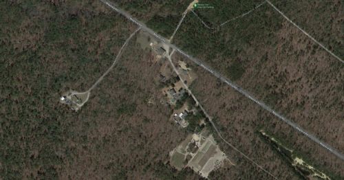 Aerial view of a wooded area with roads and scattered buildings in a rural setting.
