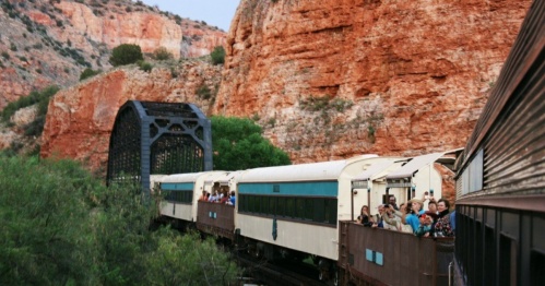 A scenic train travels through rocky terrain, with passengers enjoying the view from the open cars.