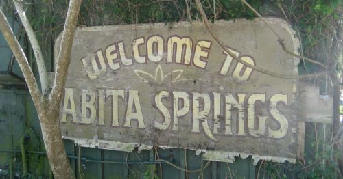 Weathered sign reading "Welcome to Abita Springs," surrounded by greenery and vines.