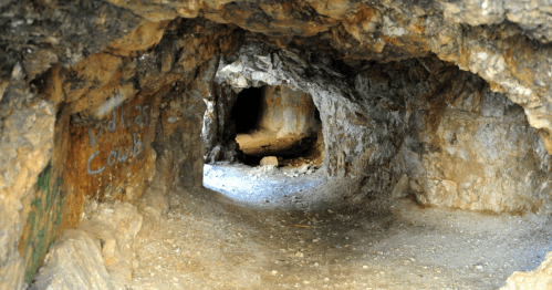 A dimly lit cave tunnel with rocky walls and a visible opening in the distance.
