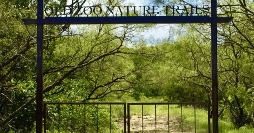 Sign for "Ole Zoo Nature Trails" at the entrance, surrounded by lush greenery and a dirt path ahead.
