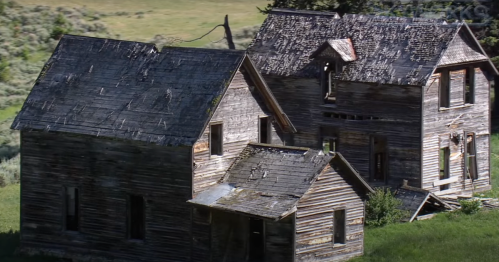 Two dilapidated wooden houses surrounded by greenery, showcasing weathered roofs and broken windows.