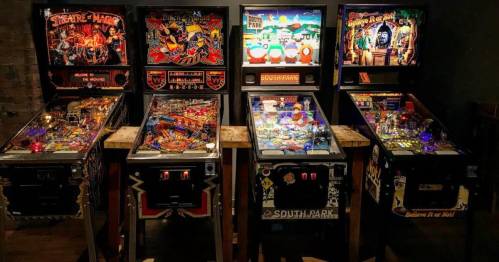 Four vintage pinball machines lined up, featuring colorful designs and themes, including "South Park" and "Medieval Madness."