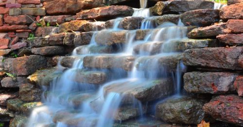 A serene waterfall cascading over smooth stone steps, surrounded by lush greenery.