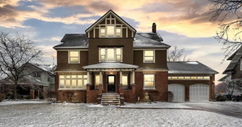 A large, elegant house with snow-covered grounds, featuring multiple windows and a welcoming entrance at sunset.