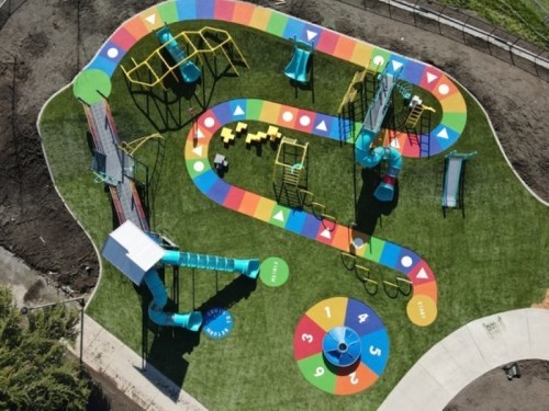 Aerial view of a colorful playground with slides, climbing structures, and a game board on grass.