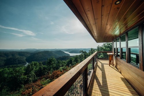 A scenic view from a wooden deck overlooking a lush landscape and a winding river under a clear blue sky.