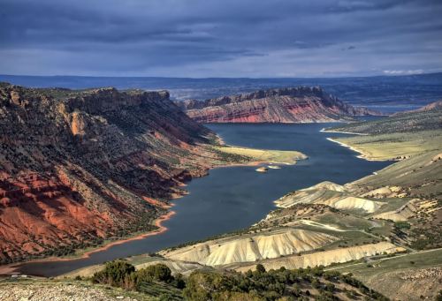 A scenic view of a winding river surrounded by colorful cliffs and rolling hills under a cloudy sky.