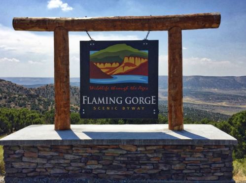 Sign for Flaming Gorge Scenic Byway, featuring a colorful landscape design, set against a mountainous backdrop.