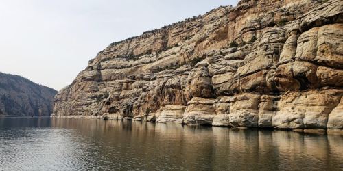 Rocky cliffs reflect in calm water, creating a serene landscape with muted colors and a tranquil atmosphere.