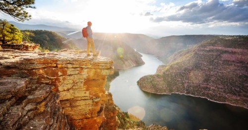 A man stands on a rocky ledge, overlooking Wyoming's Flaming Gorge at sunrise.