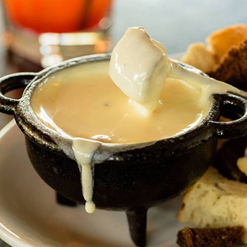 A small black pot of melted cheese with a piece of bread being dipped into it, served with assorted bread pieces.