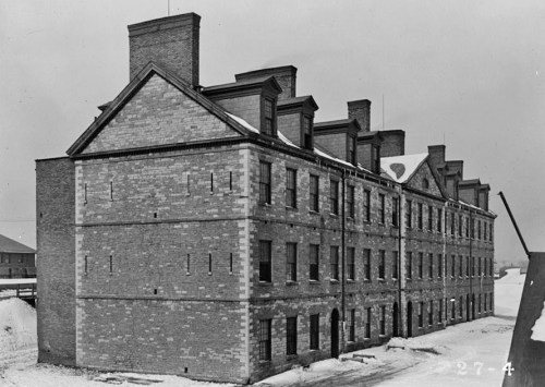 Historic black-and-white photo of a large brick building with multiple windows, set in a snowy landscape.