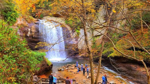 A scenic waterfall surrounded by autumn foliage, with people gathered near the water's edge.