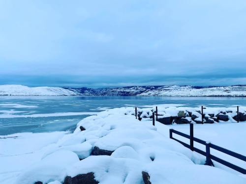 A snowy landscape with a frozen lake, mountains in the distance, and a cloudy sky.