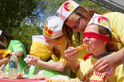 Participants in a cake-eating contest, blindfolded, enjoying their treats at an outdoor event.