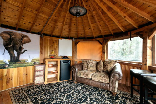 Cozy wooden gazebo interior with an elephant mural, a sofa, mini fridge, and a decorative rug.