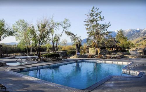 A serene outdoor pool surrounded by trees and mountains, with lounge chairs and a gazebo in the background.