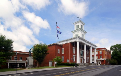 Historic building with a clock tower, columns, and flags, set against a blue sky with clouds.
