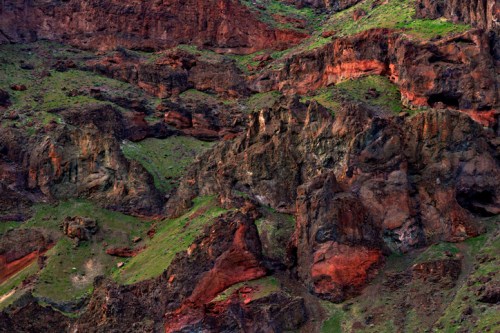 Aerial view of rugged, colorful rock formations and green vegetation in a mountainous landscape.