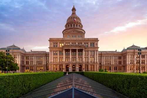 Texas State Capitol building at sunset, featuring a grand dome and landscaped gardens in the foreground.