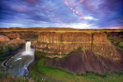 A stunning waterfall cascades down rocky cliffs, surrounded by lush greenery and dramatic clouds in the sky.