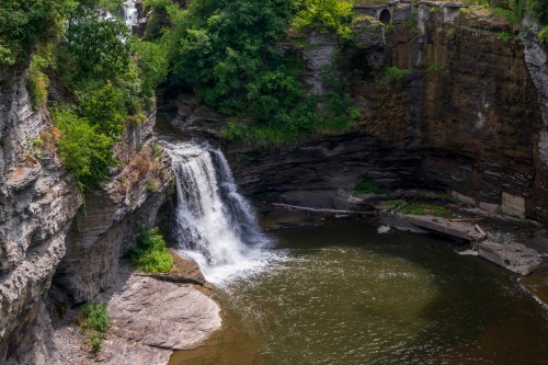 A serene waterfall cascades into a calm pool, surrounded by rocky cliffs and lush greenery.