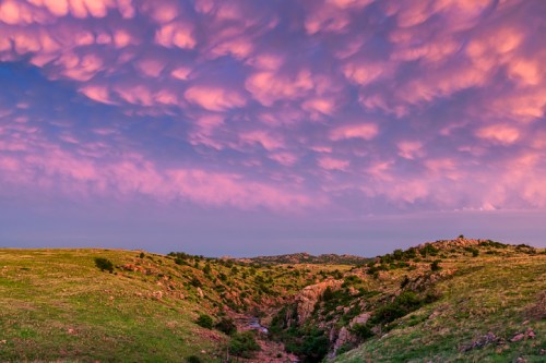 A scenic landscape featuring rolling green hills under a vibrant pink and purple sky with unique cloud formations.