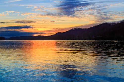 A serene sunset over a calm lake, reflecting vibrant colors on the water with hills in the background.