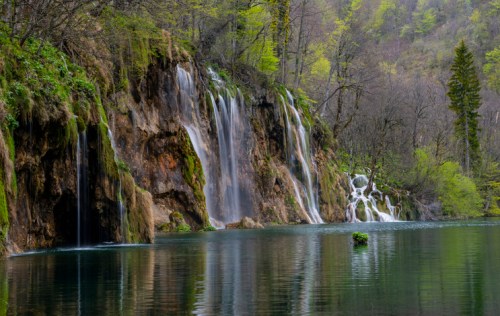 A serene landscape featuring cascading waterfalls surrounded by lush greenery and a calm, reflective lake.