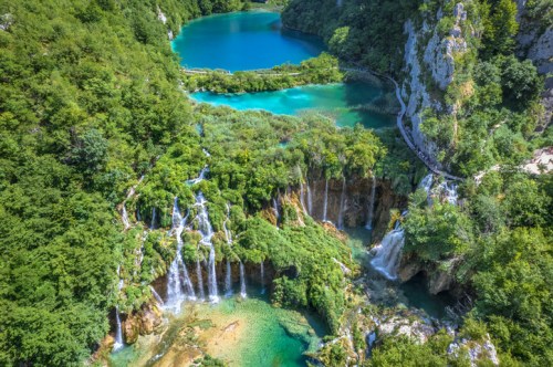 Aerial view of vibrant turquoise lakes and cascading waterfalls surrounded by lush green forests.