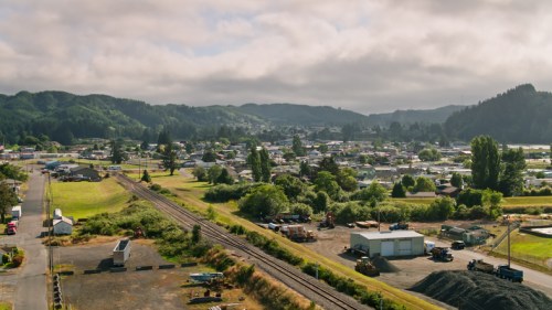 A scenic view of a small town surrounded by green hills, with railway tracks and buildings in the foreground.