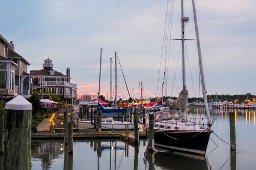 A peaceful marina at dusk, featuring sailboats docked and a charming waterfront building in the background.