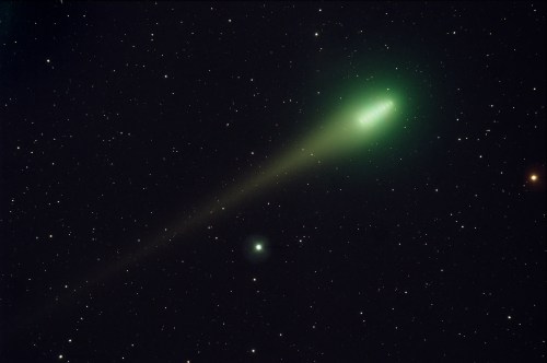 A bright green comet with a long tail against a backdrop of stars in a dark sky.