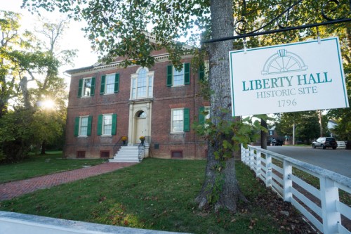 Historic brick building with green shutters, sign reading "Liberty Hall Historic Site 1796," surrounded by trees.