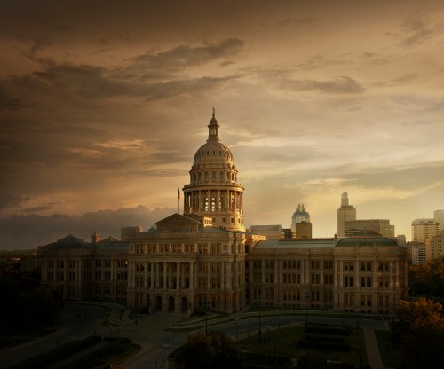 The Texas State Capitol building at sunset, with a dramatic sky and city skyline in the background.