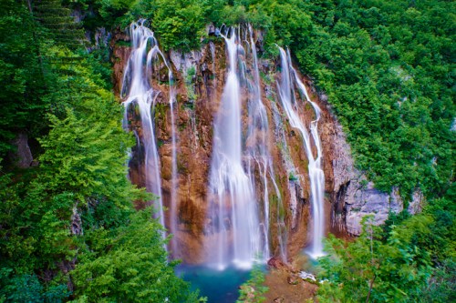 A stunning waterfall cascading down rocky cliffs, surrounded by lush green trees and a serene pool at the base.