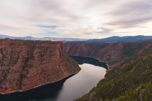 A scenic view of a winding river surrounded by steep cliffs and lush greenery under a cloudy sky.