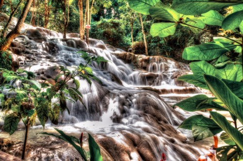 A serene waterfall cascades over rocky steps, surrounded by lush greenery and vibrant foliage.