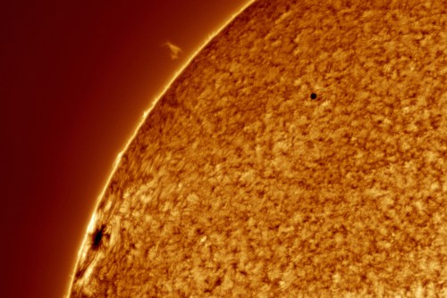 Close-up view of the sun's surface, showcasing solar textures and a small dark spot, possibly a planet or sunspot.