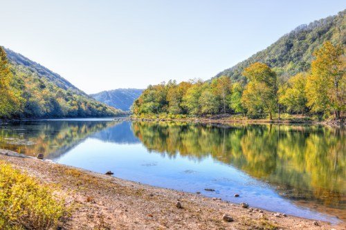 A serene river scene surrounded by lush green hills and colorful autumn trees, reflecting in calm waters.