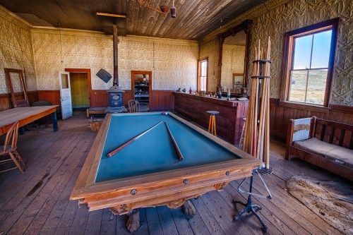 An old, rustic room featuring a billiard table, wooden furniture, and vintage decor in a historic setting.