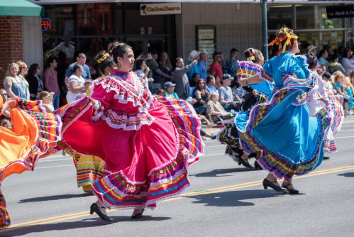 Colorful dancers in traditional dresses perform in a lively parade, showcasing vibrant costumes and joyful movement.