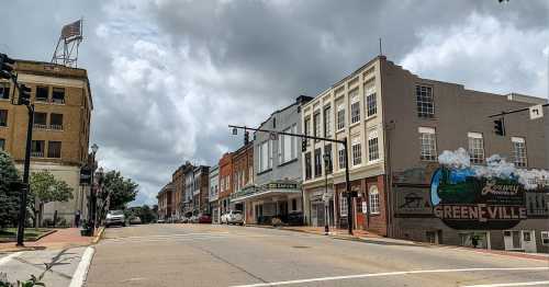 A street view of a small town with historic buildings, a mural, and cloudy skies overhead.