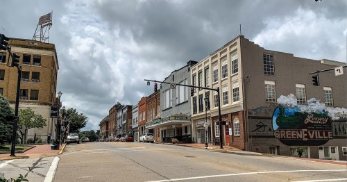 A street view of a small town with historic buildings, a mural, and cloudy skies overhead.